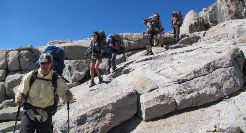 A group of backpackers hike across a large rock formation 